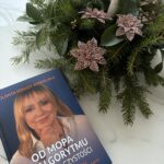 Książka "Od mopa do algorytmu - Nowa era czystości" obok świątecznej dekoracji z zielonymi gałązkami, różowymi ozdobnymi kwiatami i białą świecą na szklanym stole.